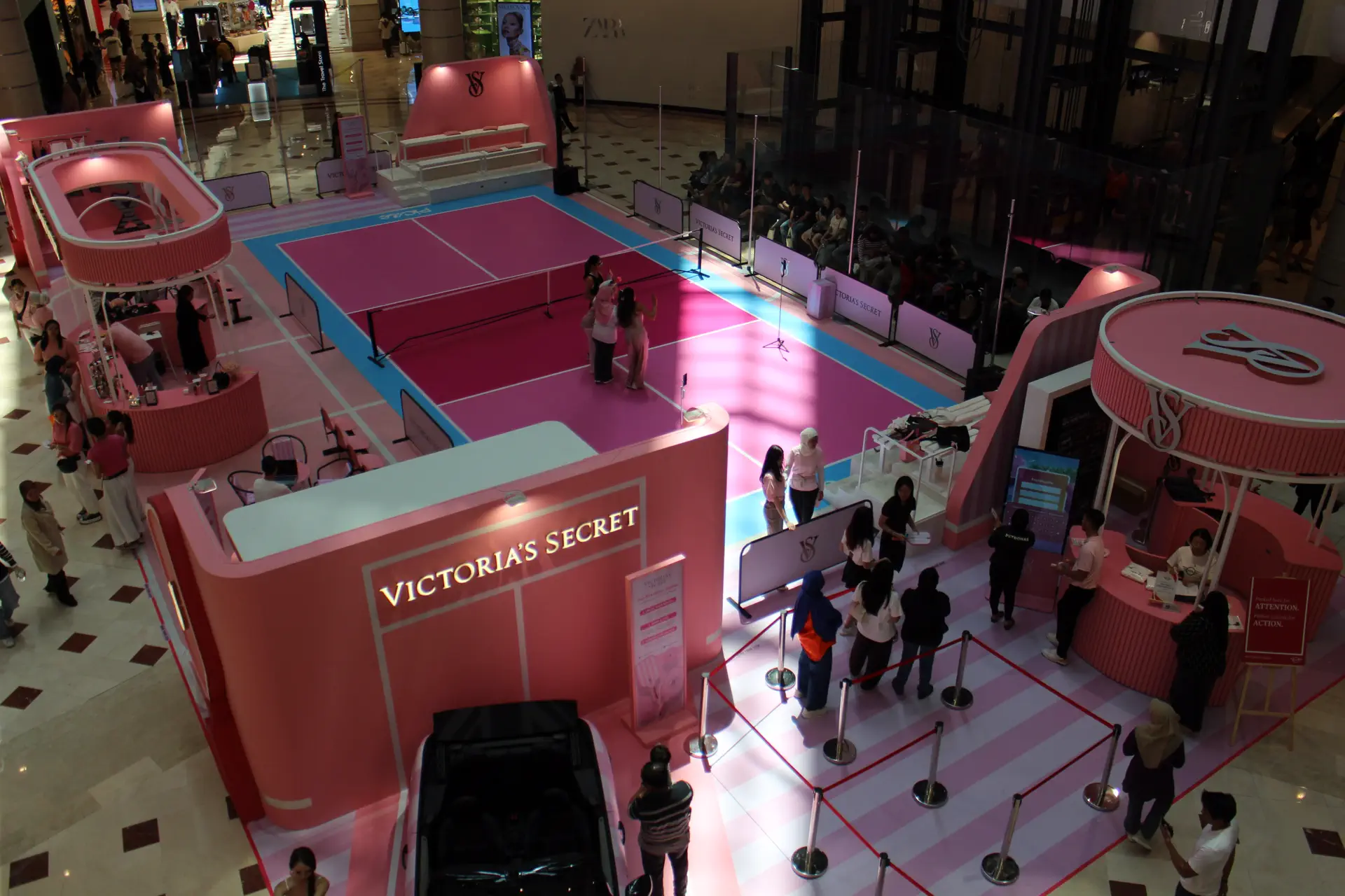 Busy mall atrium with a multi-storey glass roof, escalators and an event activation on the ground floor
